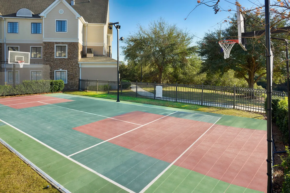 A well-maintained basketball court set amid lush greenery, with a prominent basketball hoop and clear court markings. The energetic mood invites friendly matches and active gatherings.