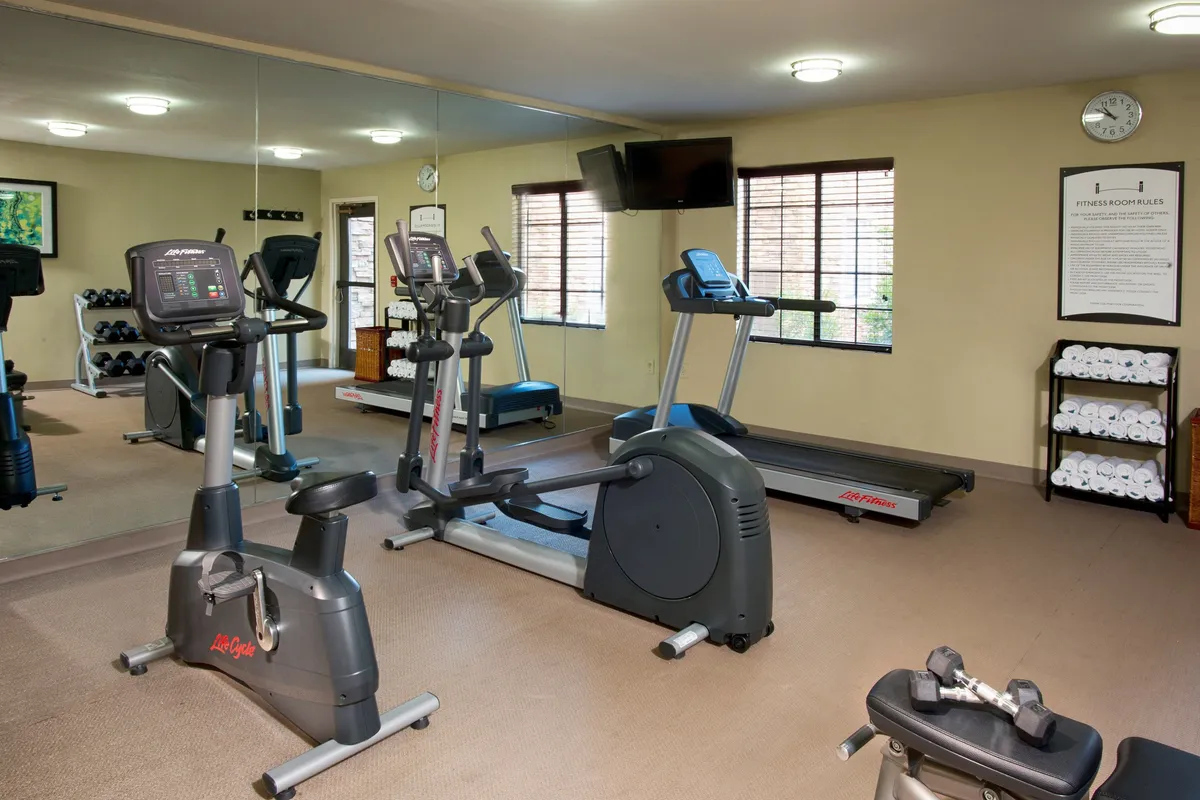 A modern fitness center featuring exercise bikes, a treadmill, dumbbells, and large mirrors. The room is bright and motivational, with equipment arranged for both solo workouts and group fitness.