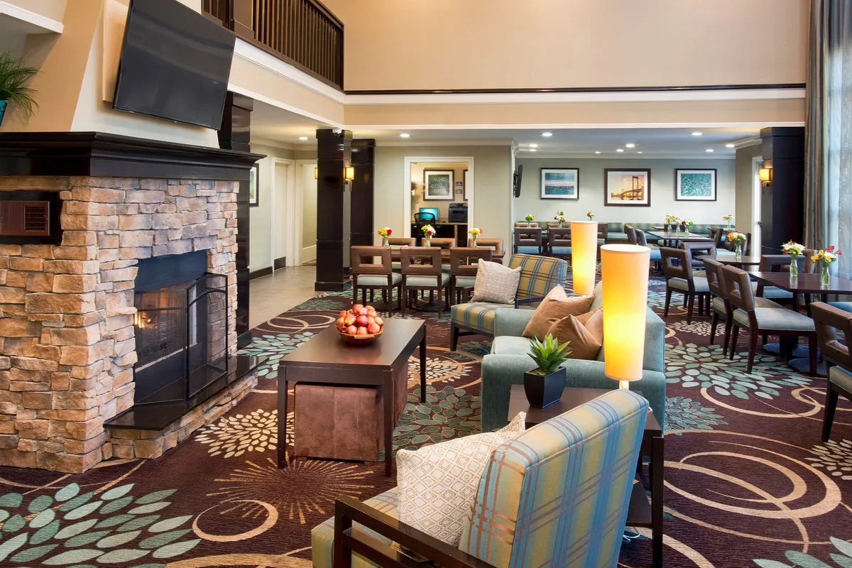 A warm, inviting living space with a fireplace, comfortable seating area, decorative artwork, and an adjacent dining area. The atmosphere is homely and ideal for social gatherings, relaxation, and shared meals, reflecting the comfort and flexibility of suite-style living.