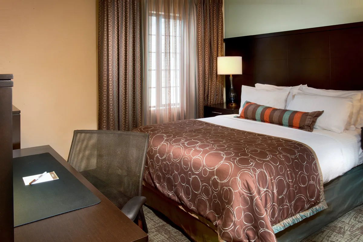 A cozy bedroom featuring a comfortable queen-size bed, a desk perfect for work or reading, soft curtains, and a warm bedside lamp. The room is styled in soothing tones, inviting relaxation and peaceful rest.