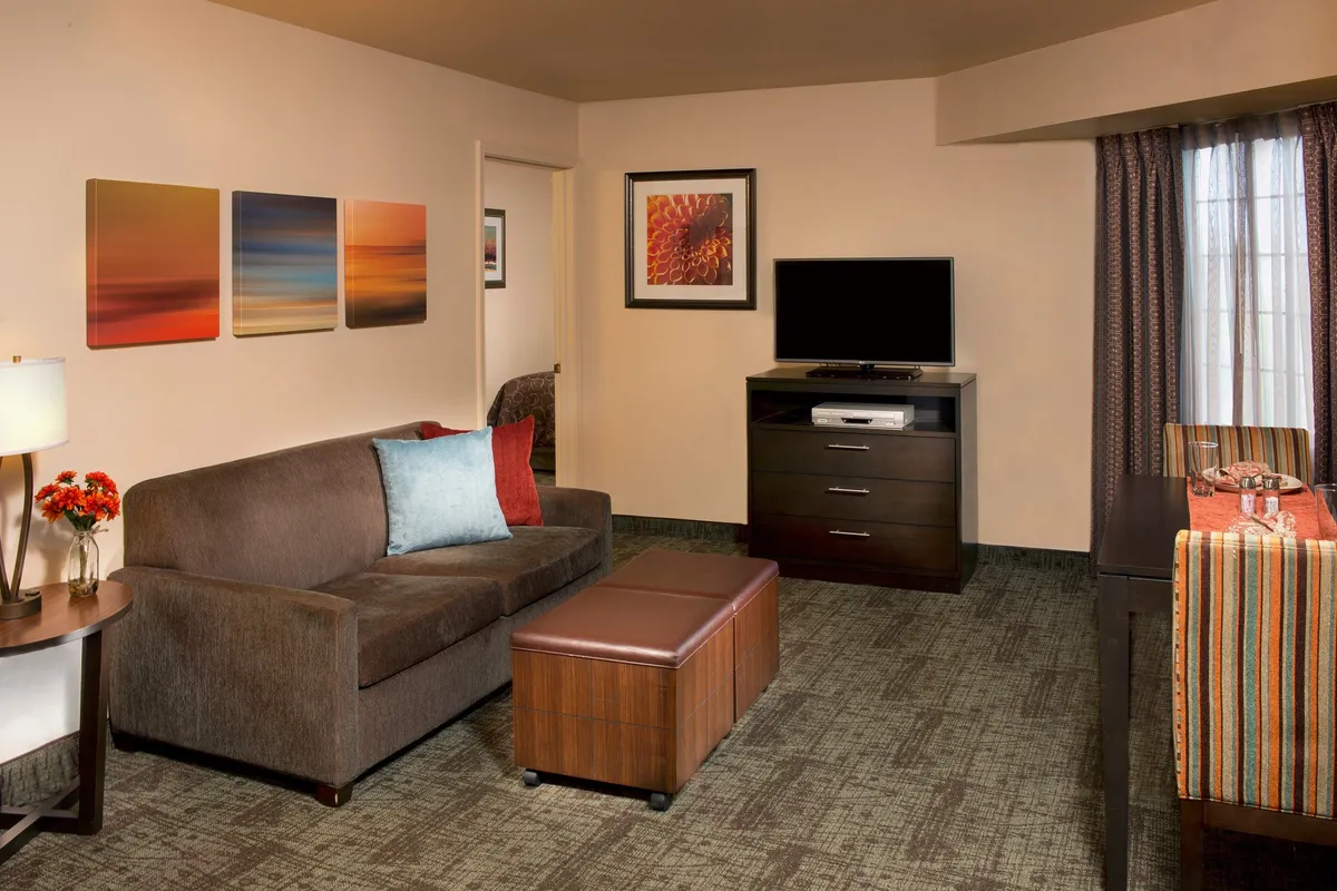 The image showcases the condo’s inviting living area, featuring a plush sofa facing a large television, modern artwork on the walls, a stylish coffee table, and a dining space set for a cozy meal. The scene exudes warmth and comfort, perfect for gathering with friends or family.
