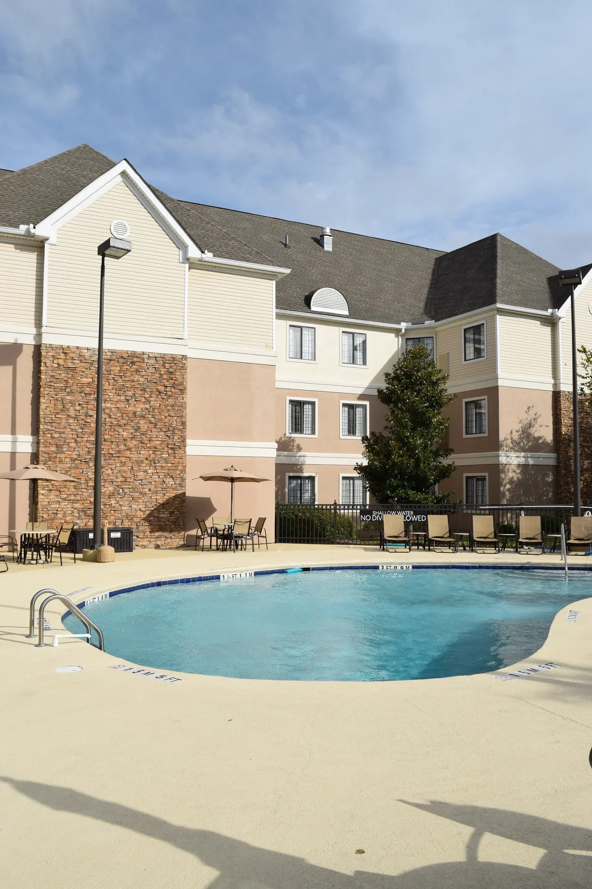 A spacious outdoor swimming pool surrounded by lounge chairs and umbrellas, set against the backdrop of the hotel exterior. Guests appear to be enjoying a relaxing day by the pool, with some sunbathing and others socializing. The scene radiates a warm, inviting atmosphere, perfect for family downtime after busy outings.