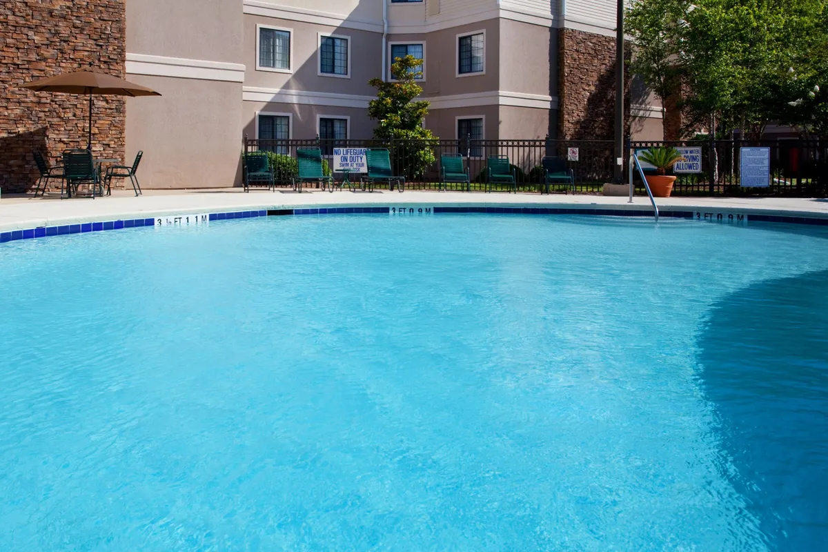 A tranquil exterior view showcasing a large swimming pool with inviting poolside chairs, all set against the building’s facade. The scene is bathed in warm, relaxing light, suggesting a serene environment for sunset swims and social gatherings by the water.