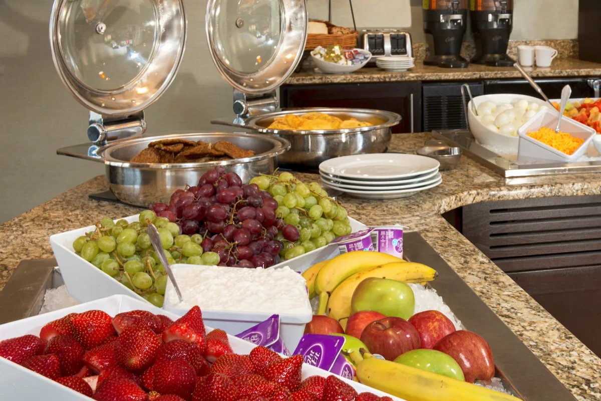 A cheerful breakfast setup with trays of hot food, a vibrant fruit display, and a well-stocked coffee station. The setting is lively, with guests preparing to enjoy their morning meal, reflecting a relaxed yet energetic start to the day.
